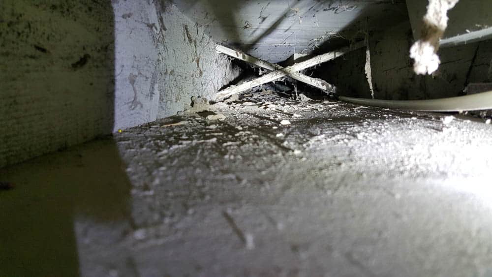 Photo looking into a return air duct before cleaning shows thick dust and debris built up.
