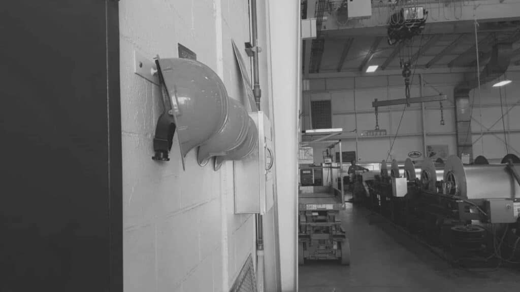 Black and white photo of hard hats hanging on a wall in the sheet metal shop.