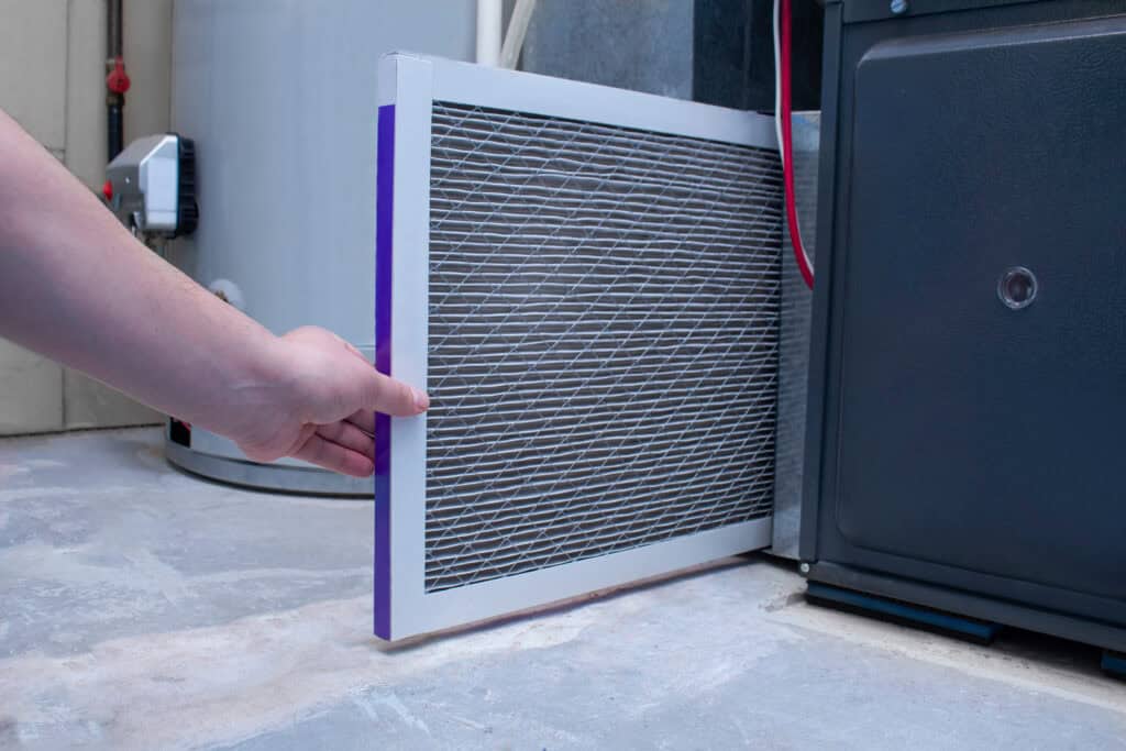 A person changing an air filter on a high efficiency furnace that is blowing cold air