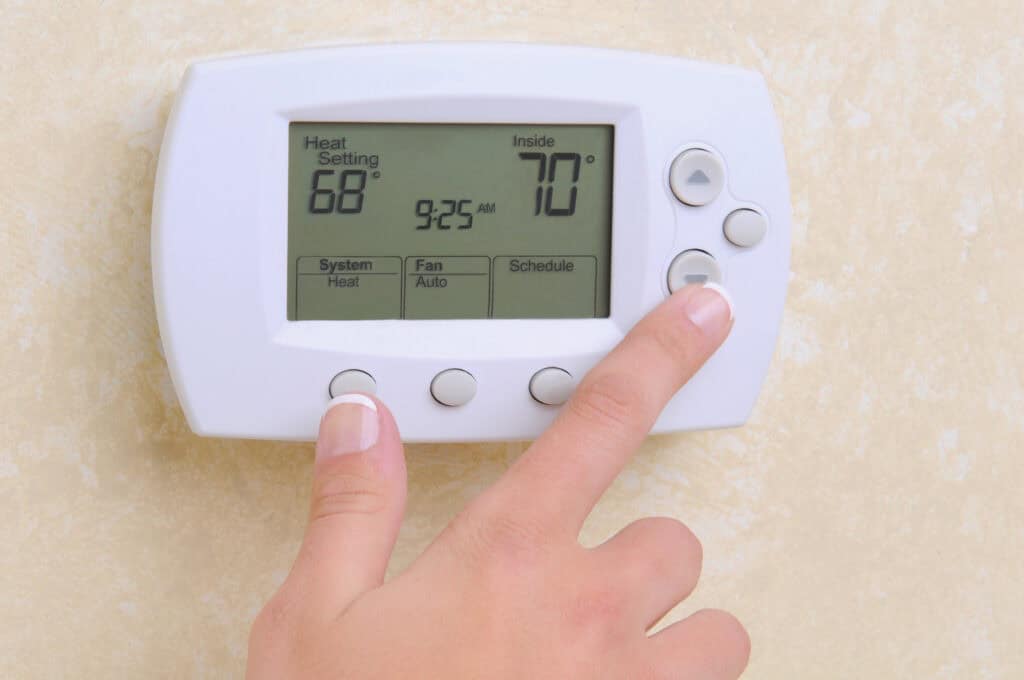 Closeup of a womans hand setting the room temperature on a modern programable thermostat to check why is my furnace blowing cold air