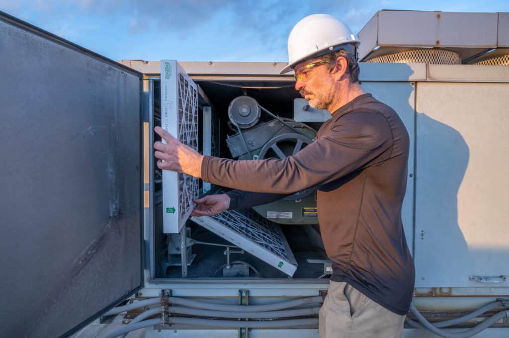 man standing in front of an exterior HVAC using changing the filter for Preventative Maintenance On A Commercial HVAC