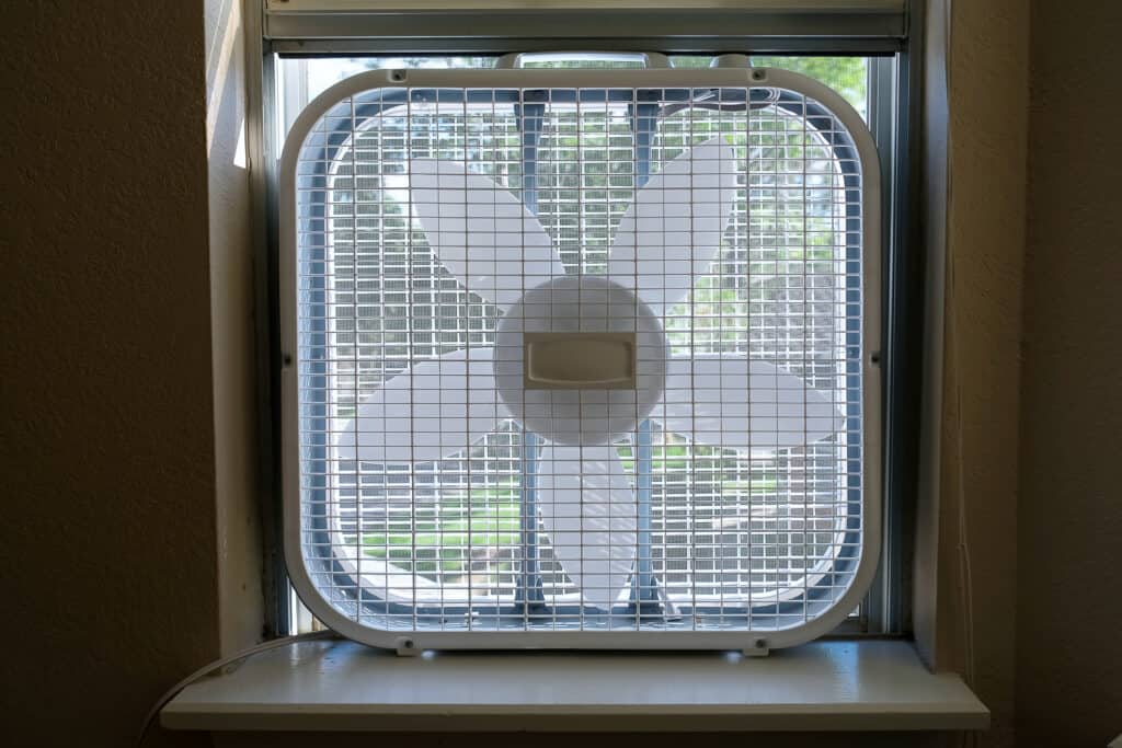 Classic window box fan inserted in home room window indoor how to keep house cool without ac