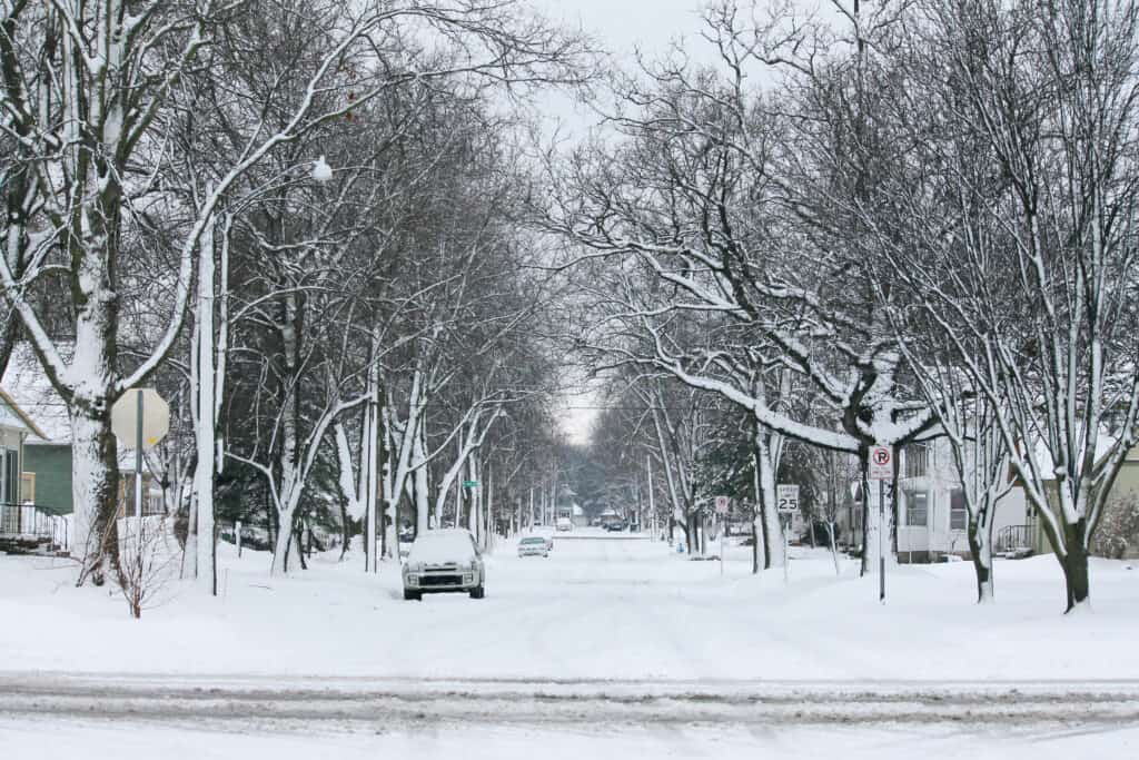 fresh white snow covering a residential street in Iowa. trees lining street, car parked in street. cold winter day
