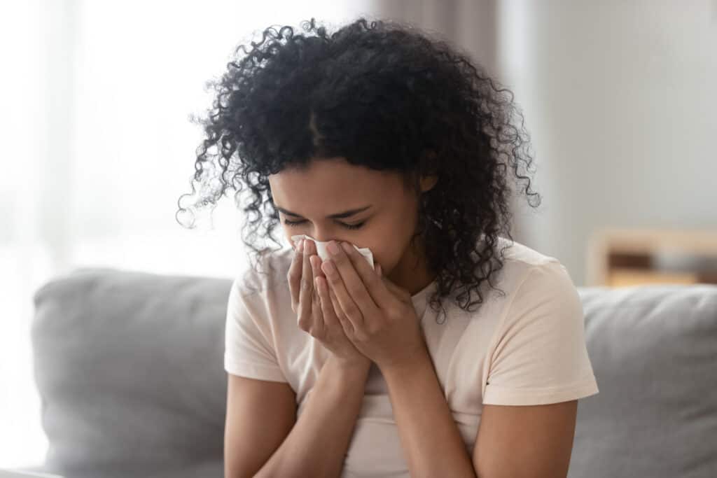 woman dealing with seasonal allerigies indoors, sitting on couch, blowing nose, needs indoor air quality services
