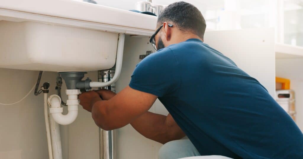 man doing plumbing maintenance work under bathroom sink